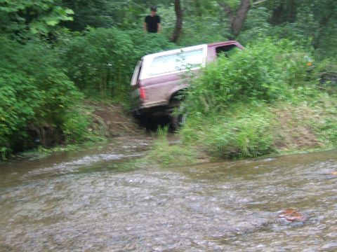 1993 Ford Bronco - A person watches as a Ford Bronco navigates a stream in a wooded area.