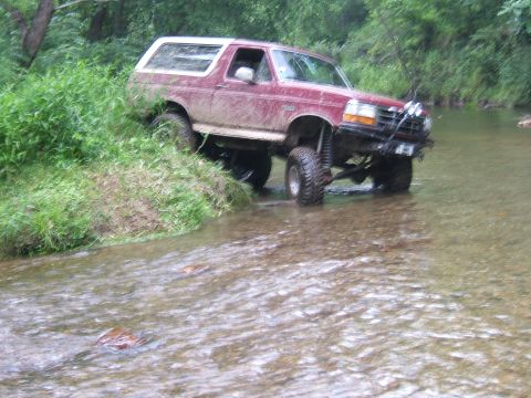 1993 Ford Bronco - This lifted 1993 Ford Bronco navigates a shallow stream, its off-road tires gripping the rocky bed.
