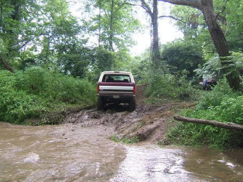 1993 Ford Bronco - A 1993 Ford Bronco navigates a challenging muddy trail with another vehicle visible in the background.