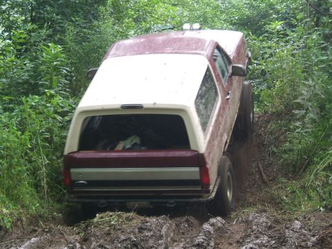 1993 Ford Bronco - This Ford Bronco is navigating a challenging muddy off-road path surrounded by dense green foliage.