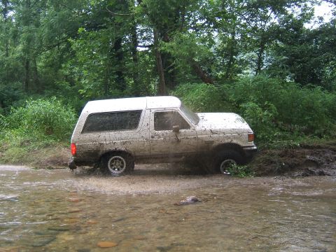 1993 Ford Bronco - A white 1992 Ford Bronco navigates a muddy stream, kicking up water and mud.