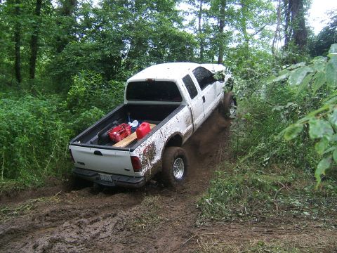 1993 Ford Bronco - A white pickup truck navigates a muddy trail surrounded by dense green foliage.