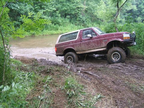1993 Ford Bronco - 1993 Ford Bronco driving through a muddy, wooded area near a creek.
