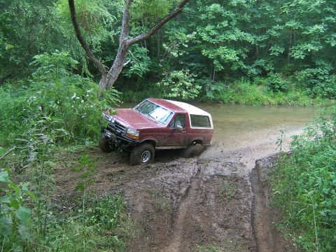 1993 Ford Bronco - 1993 Ford Bronco navigating a challenging muddy terrain with water present.