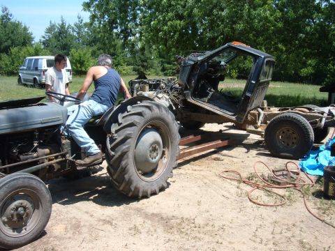1985 Ford F-150 - A tractor is being used to move a truck chassis that has been stripped down.