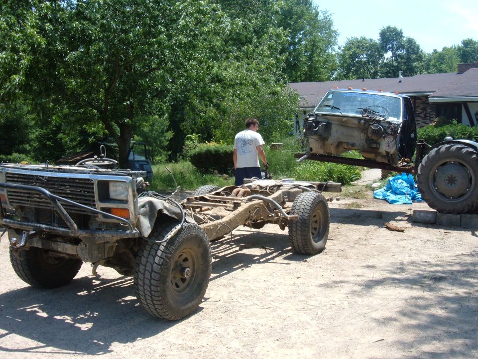 Truck chassis with custom bumper and a cab being lifted by a tractor