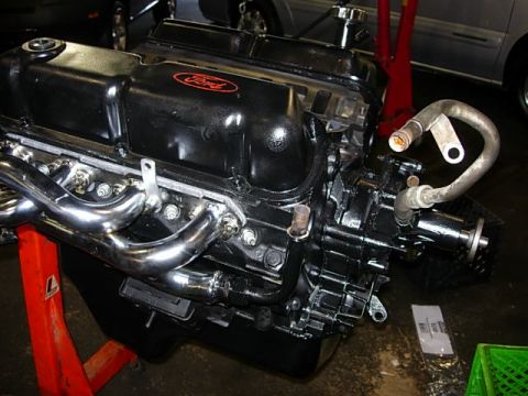 1993 Ford Bronco - A black Ford engine with a chrome exhaust manifold is displayed on a red engine stand.