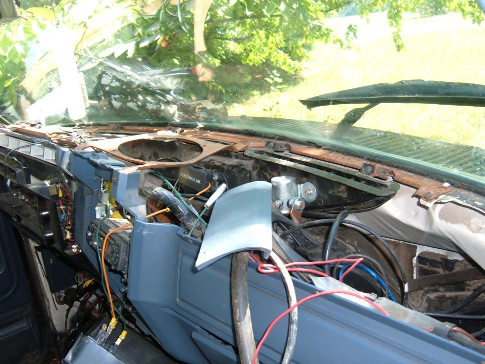 Disassembled dashboard with exposed wires and components. A metal rod supports a gray panel