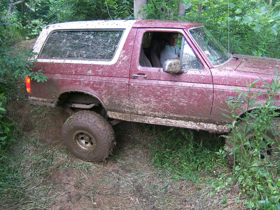 Mud-covered maroon 1992 Ford Bronco with a white top, driving off-road