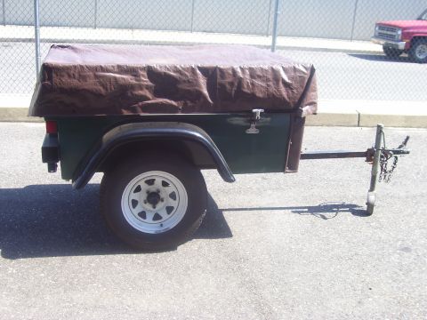 1991 Ford Bronco - Side view of a small single-axle utility trailer with a dark green steel tub, black fenders, and white five-spoke wheels, its load covered…