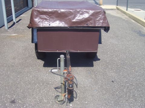 1991 Ford Bronco - Front view of a small single-axle utility/tent trailer covered with a brown tarp and a brown fabric front panel, parked on asphalt. The rus…
