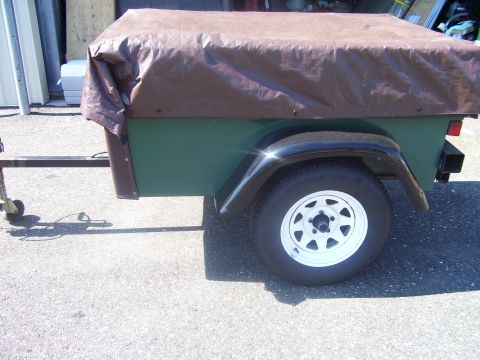 1991 Ford Bronco - Side view of a small single-axle utility trailer with a green box, black fender and brown tarp stretched over the load, parked on asphalt o…