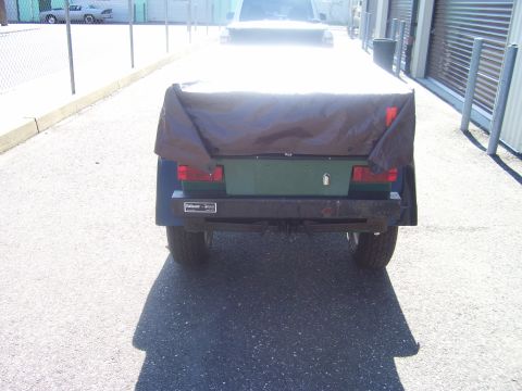 1991 Ford Bronco - Rear view of a small green single-axle utility trailer covered with a brown tarp, showing red tail lights, a license-plate light and a rust…