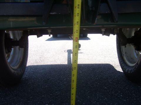 1991 Ford Bronco - Low-angle shot from behind a green truck body measuring ride height with a yellow tape measure stretched from the frame rail down to the as…