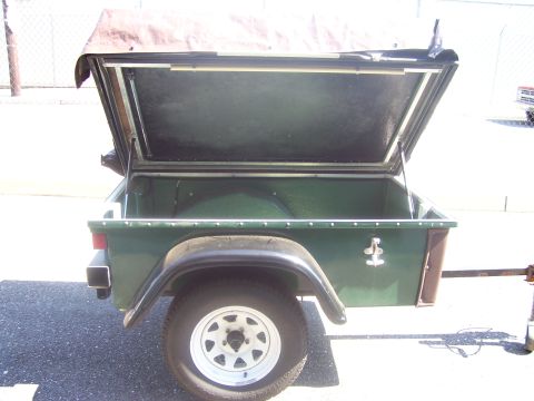 1991 Ford Bronco - A small green single-axle utility trailer photographed from the rear, with its lid/hood propped open to reveal an empty painted interior. I…