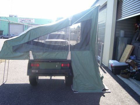 1991 Ford Bronco - Rear view of a small utility trailer with a green tent camper deployed and open, showing mesh windows and a support pole, parked on pavemen…