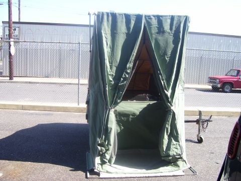 1991 Ford Bronco - A green canvas tent or shelter, likely a military-style camping enclosure, set up in a paved parking lot with a trailer hitch visible at ri…