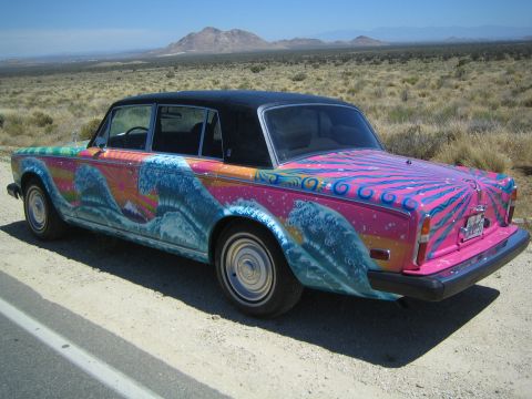 1968 Ford Mustang - A custom painted sedan with a vibrant wave and sunburst design is parked on a dusty roadside.