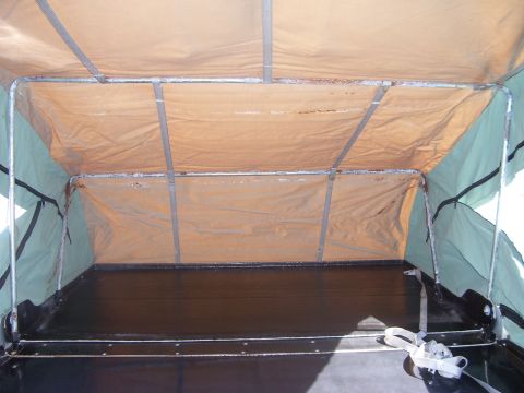 1991 Ford Bronco - Interior view of a canvas tent camper setup, showing tan fabric walls with metal support poles, dark green side panels, a dark floor, and a…