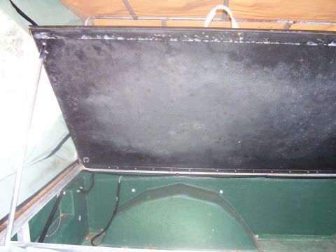1991 Ford Bronco - Interior of a small green utility trailer with the lid propped open, showing the weathered black underside of the hinged lid, riveted edge…