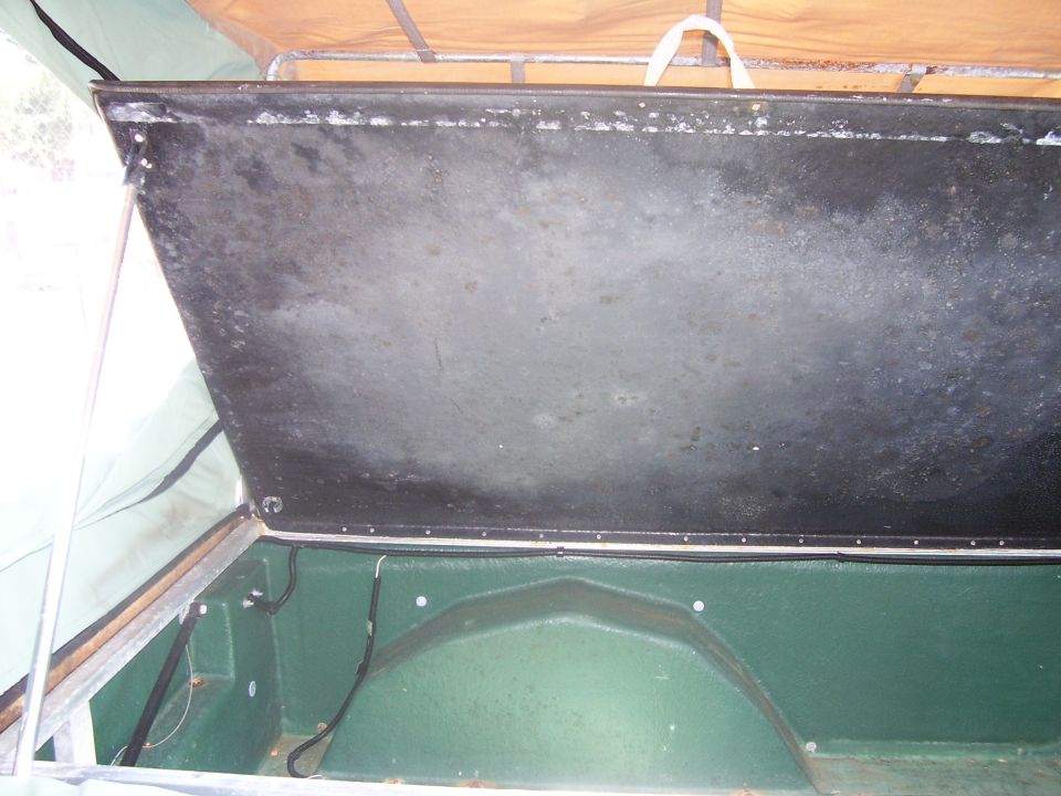 Open lid of a green utility trailer showing weathered black underside and empty tub