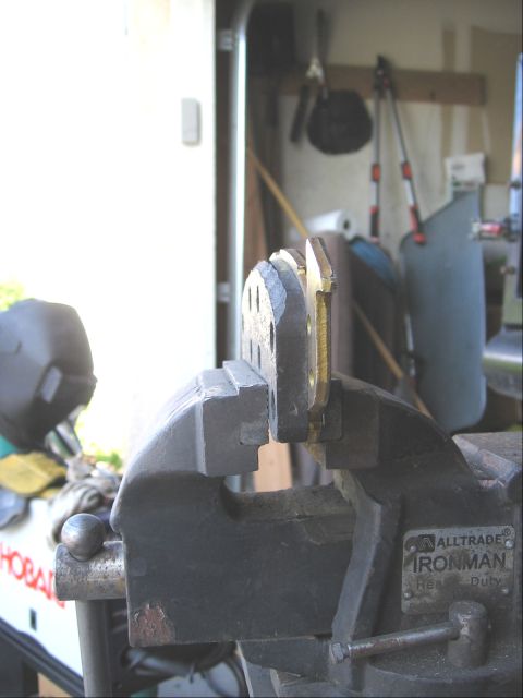 1994 Ford Bronco - A metal component is secured in a heavy-duty vise, ready for work in a garage setting.