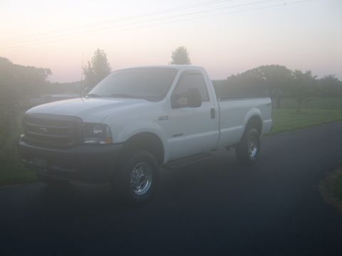 2003 Ford F-250 - A white 2003 Ford F-250 pickup truck is seen from a 3/4 front angle on a road with trees and fog in the background.