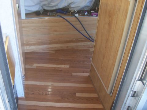 1994 Ford F-150 - Interior of a trailer or RV during a hardwood floor installation, showing newly laid oak strip flooring running up a raised step area next…
