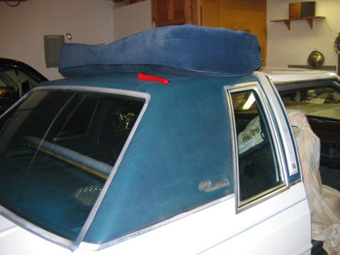 1985 Ford LTD Crown Victoria - A blue cushion is placed on the roof of a white car, with a red emergency flasher nearby.