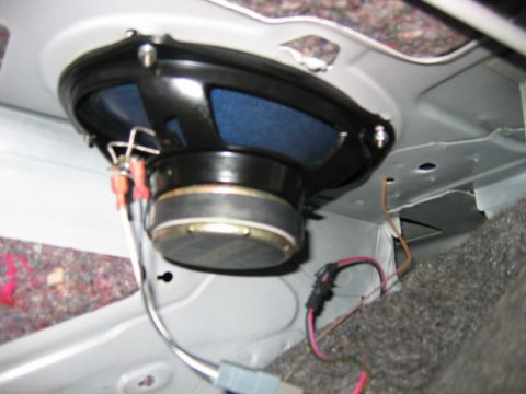 1985 Ford LTD Crown Victoria - Close-up of an oval speaker mounted in a rear deck or panel, showing the black speaker basket with blue cone and exposed wiring including r…