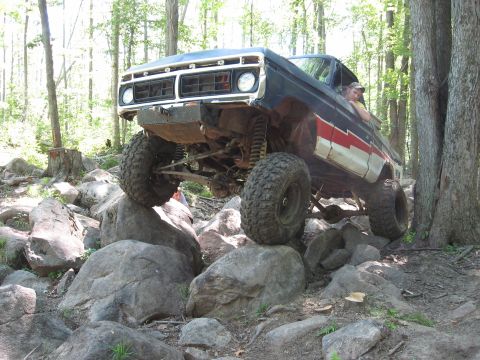 1977 Ford F-150 - This modified pickup truck is navigating a challenging rocky terrain in a forest setting.