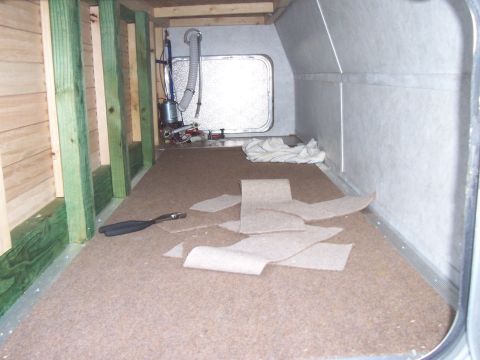 1994 Ford F-150 - The interior of a camper shell shows unfinished wood framing, a window, and carpet pieces scattered on the floor.
