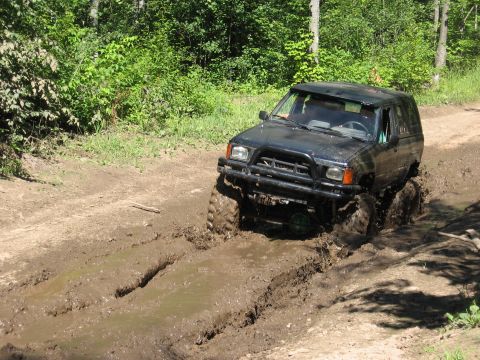 1977 Ford F-150 - Off-road SUV struggles through deep mud on a wooded trail.