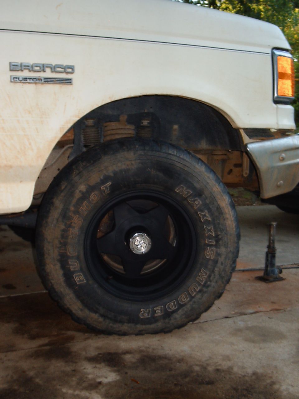 Front wheel of a white Ford Bronco Custom with black wheel and Maxxis Buckshot Mudder tire