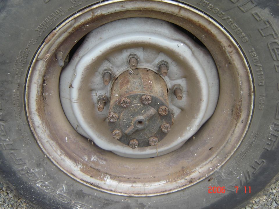 Close-up of a rusty wheel hub with lug nuts and a tire. Tire has text 'LT235/85R16'