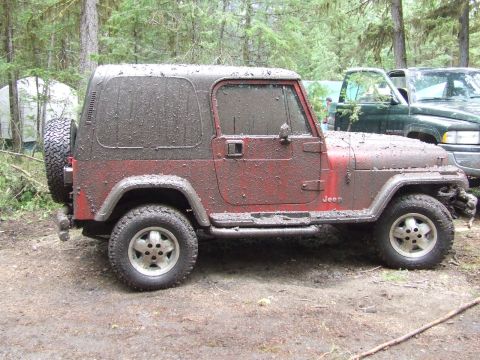 1990 Ford Bronco - This Jeep is covered in mud, suggesting it has been off-roading. Another vehicle and camping gear are visible in the background.