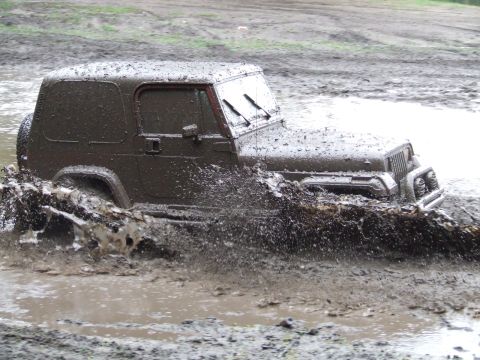 1990 Ford Bronco - A Jeep Wrangler navigates a muddy obstacle course, sending mud flying.