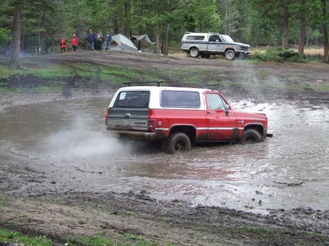 1990 Ford Bronco - Off-roading adventure with two SUVs in a muddy forest setting.