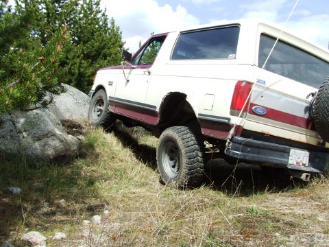 1990 Ford Bronco - This 1990 Ford Bronco is navigating a rocky, off-road trail with trees in the background.
