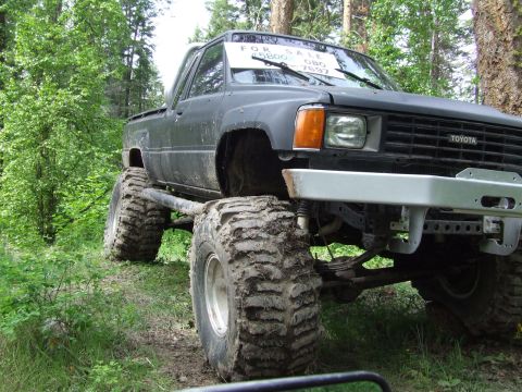 1990 Ford Bronco - A heavily modified Toyota pickup truck sits off-road with oversized tires and a 'For Sale' sign visible through the windshield.