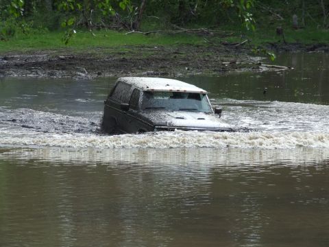 1990 Ford Bronco - SUV navigates through a muddy water crossing, kicking up a significant splash.