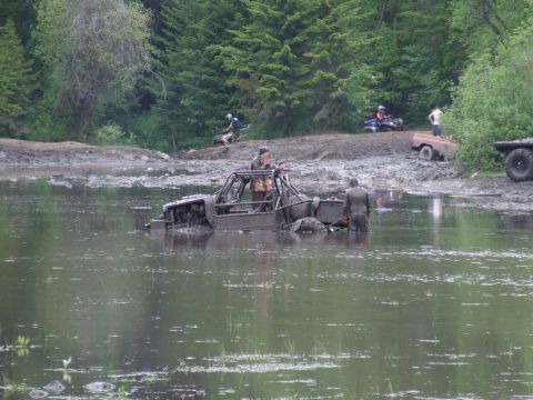 1990 Ford Bronco - Off-road vehicles navigate a muddy terrain and waterlogged area during an event.