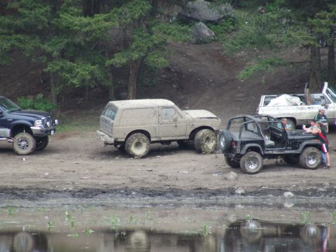 1990 Ford Bronco - Several off-road vehicles are parked near a body of water after an event.