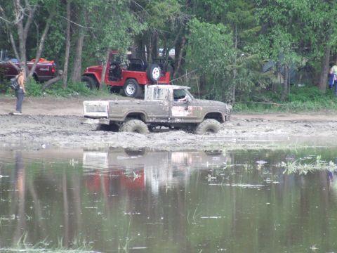 1990 Ford Bronco - A muddy pickup truck is stuck in a waterlogged area with a red Jeep behind it.