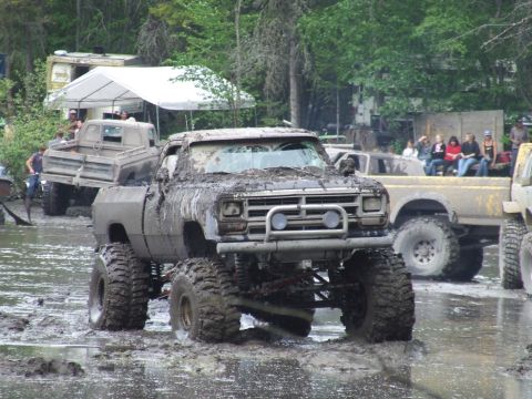 1990 Ford Bronco - Several mud-covered trucks are in a muddy area, with people watching in the background.