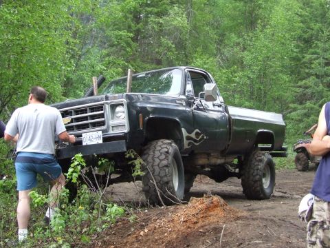 1990 Ford Bronco - A lifted black 1973 Chevrolet pickup truck is shown off-road with an ATV in the background.