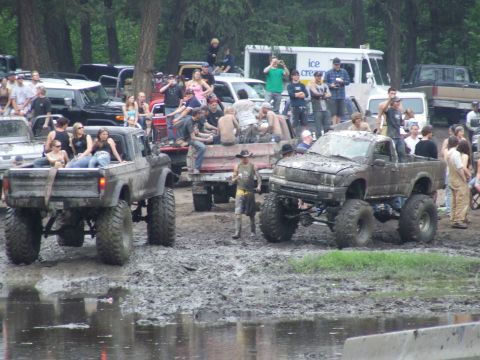 1990 Ford Bronco - Muddy pickup trucks with people gathered around at an outdoor event.