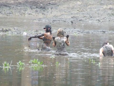 1990 Ford Bronco - Several individuals are wading and playing in a muddy body of water, covered in mud.
