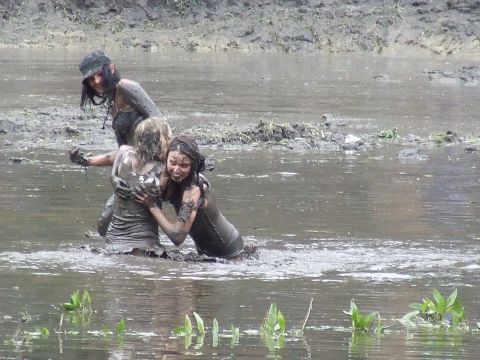 1990 Ford Bronco - Three individuals covered in mud interact in a muddy body of water, possibly during an outdoor event.