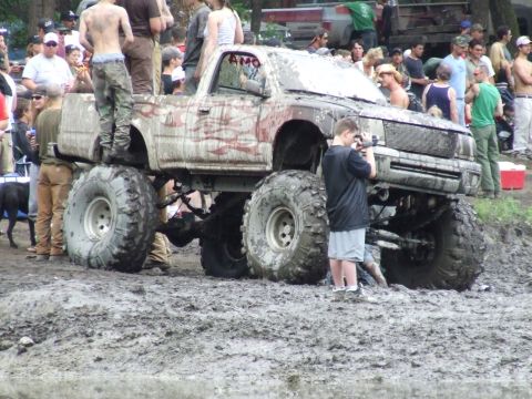 1990 Ford Bronco - A heavily modified pickup truck is stuck in the mud with onlookers present.